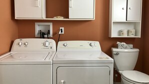Uma área de lavanderia com duas máquinas de lavar, um sanitário e um armário com artigos de higiene pessoal.