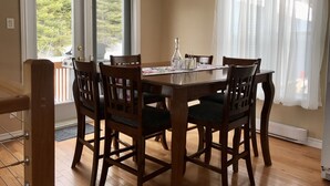 Uma área de refeições com mesa e cadeiras de madeira, uma janela com vista para árvores e uma porta que dá para uma varanda.