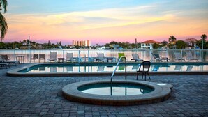 Ett poolområde med solstolar och en bubbelpool, omgivet av en gångväg av tegel och ett staket av metall.