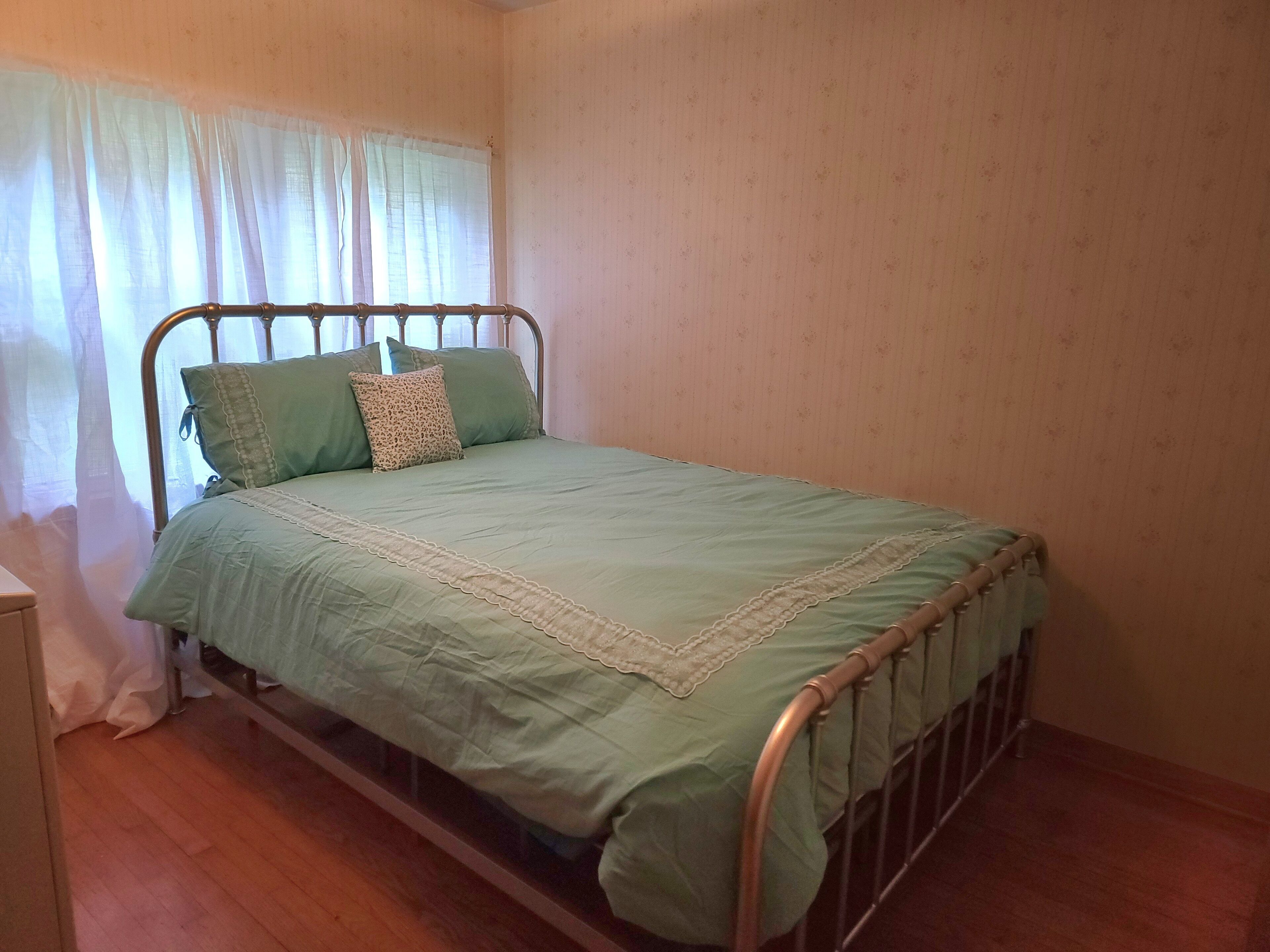 Un lit simple avec un cadre en métal, une couvre-lit verte et deux oreillers.