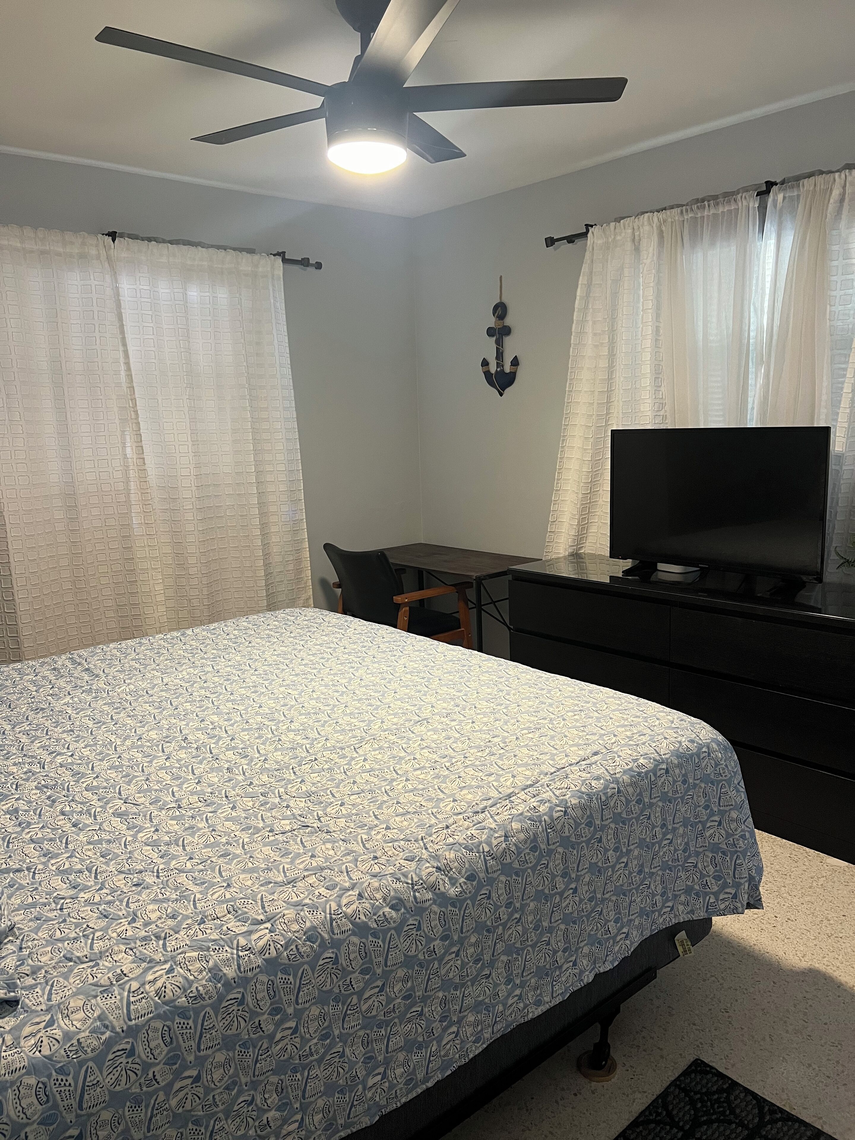 Ein Schlafzimmer mit Bett, Schreibtisch, Fernseher und Deckenventilator.