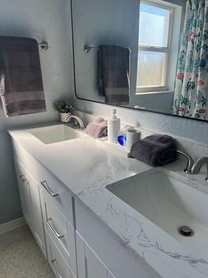 Un baño con dos lavamanos, un espejo y una ventana con cortinas.