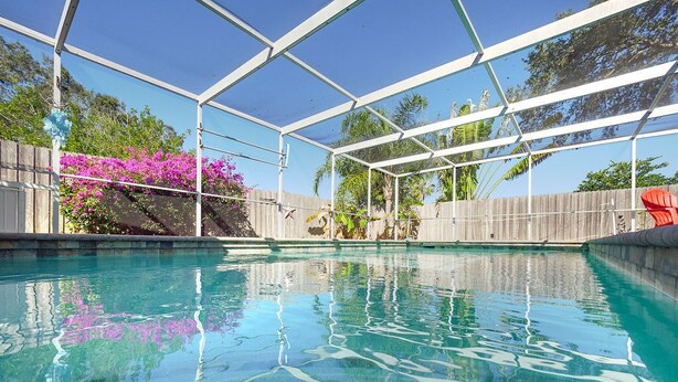 Una piscina cristalina con piso de baldosas, rodeada por una valla de madera y un área techada con estructura metálica.
