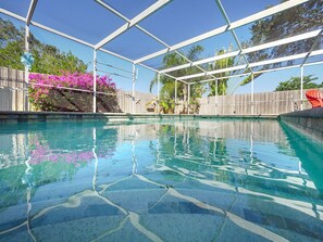 En klar swimmingpool med flisegulv, omgivet af et træhegn og et overdækket område med metalramme.