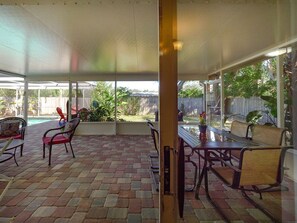 Un porche cubierto con suelo de ladrillo, mobiliario exterior y vista a un jardín trasero.