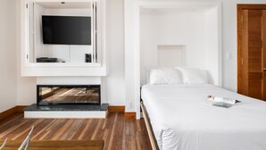 A modern hotel room with a large bed, a flat-screen TV mounted on a white wall, and a wooden floor.