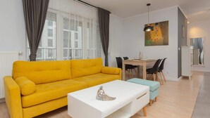 A modern living room with a yellow sofa, a white coffee table, and a dining area with a table and chairs.