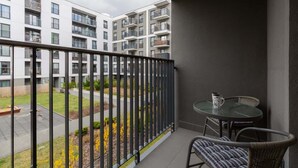 A balcony with a glass table and chairs, overlooking a courtyard with a building in the background.