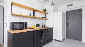 Eine moderne Küche mit schwarzen Schränken, einer Mikrowelle, Holzregalen und einer Backspüle mit Fischgrätmuster.
