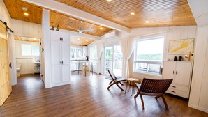 A spacious room with wooden flooring, a dining area with a table and chairs, and a kitchen in the background. - Family Accessible Lakehouse (Westport)