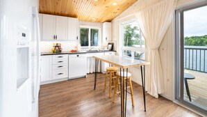 A modern kitchen with white cabinets, a wooden ceiling, and a large window overlooking a body of water. - Family Accessible Lakehouse (Westport)