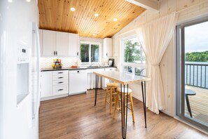 Eine moderne Küche mit weißen Schränken, einer Holzbalkendecke und einem großen Fenster mit Blick auf ein Gewässer.