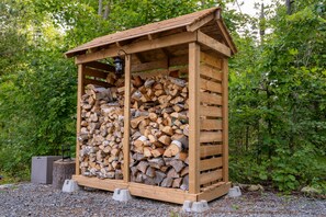 Un abri en bois, doté d’un toit incliné, où est rangé avec soin une pile de bois de chauffage.