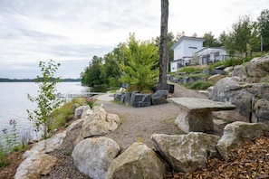 Ein Haus am See mit Kiesweg, großen Felsen und einer Terrasse.