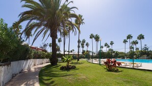 Un área de piscina con palmeras, un camino de baldosas y un césped.