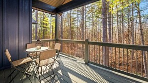 A covered outdoor deck with a table and chairs, overlooking a forest.