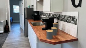 Eine moderne Küche mit weißen Schränken, einer Holz Arbeitsplatte, einer schwarzen Kaffeemaschine und einer gefliesten Spritzschutzwand.
