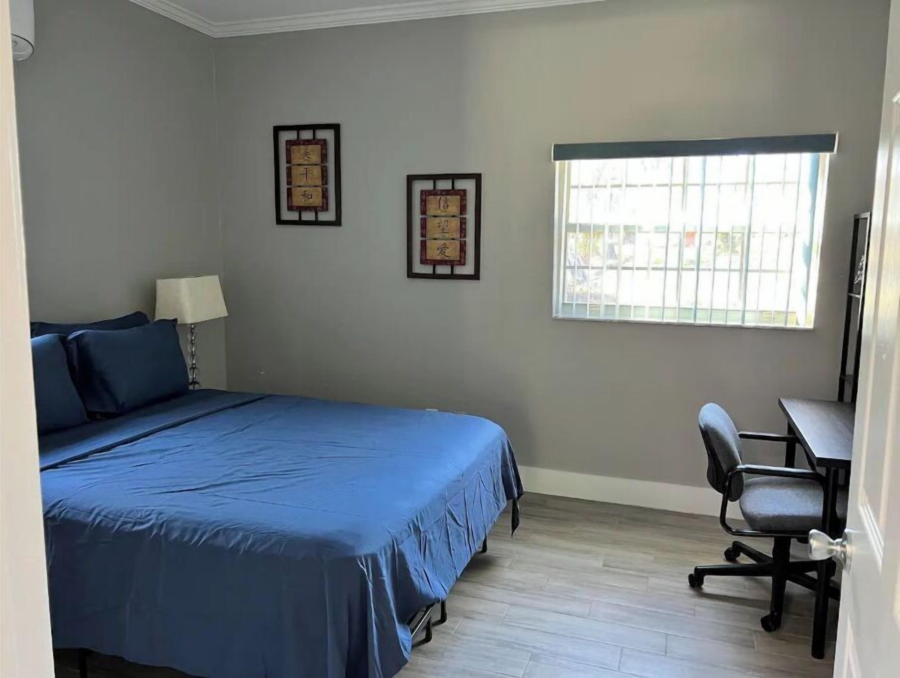 A bedroom with a bed, a desk, and two framed items on the wall.