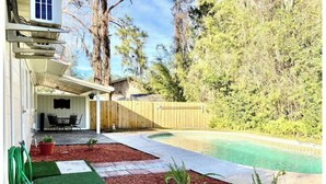 Ein Garten mit Pool, einer überdachten Terrasse und einem Holzzaun.