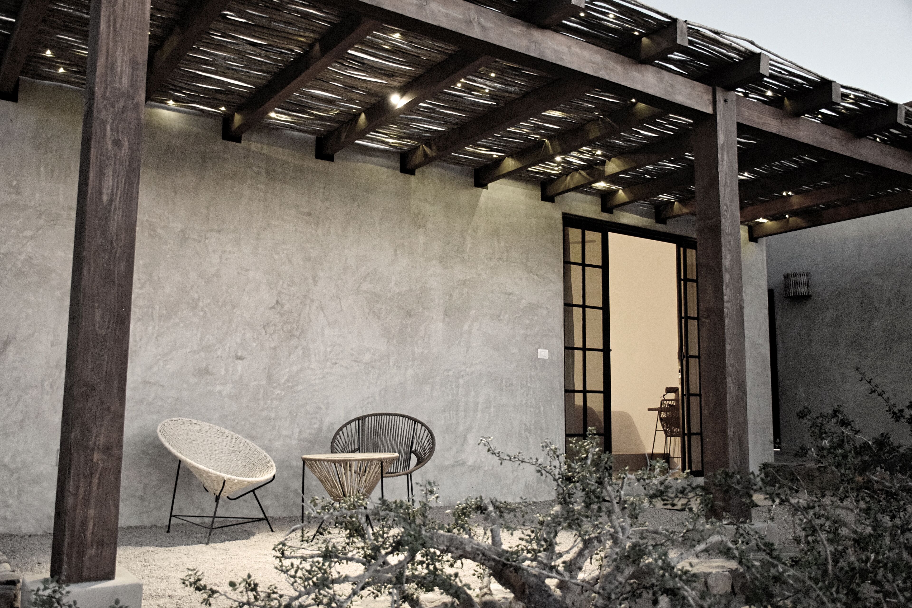An outdoor patio area with two chairs, a pergola, and a concrete wall.