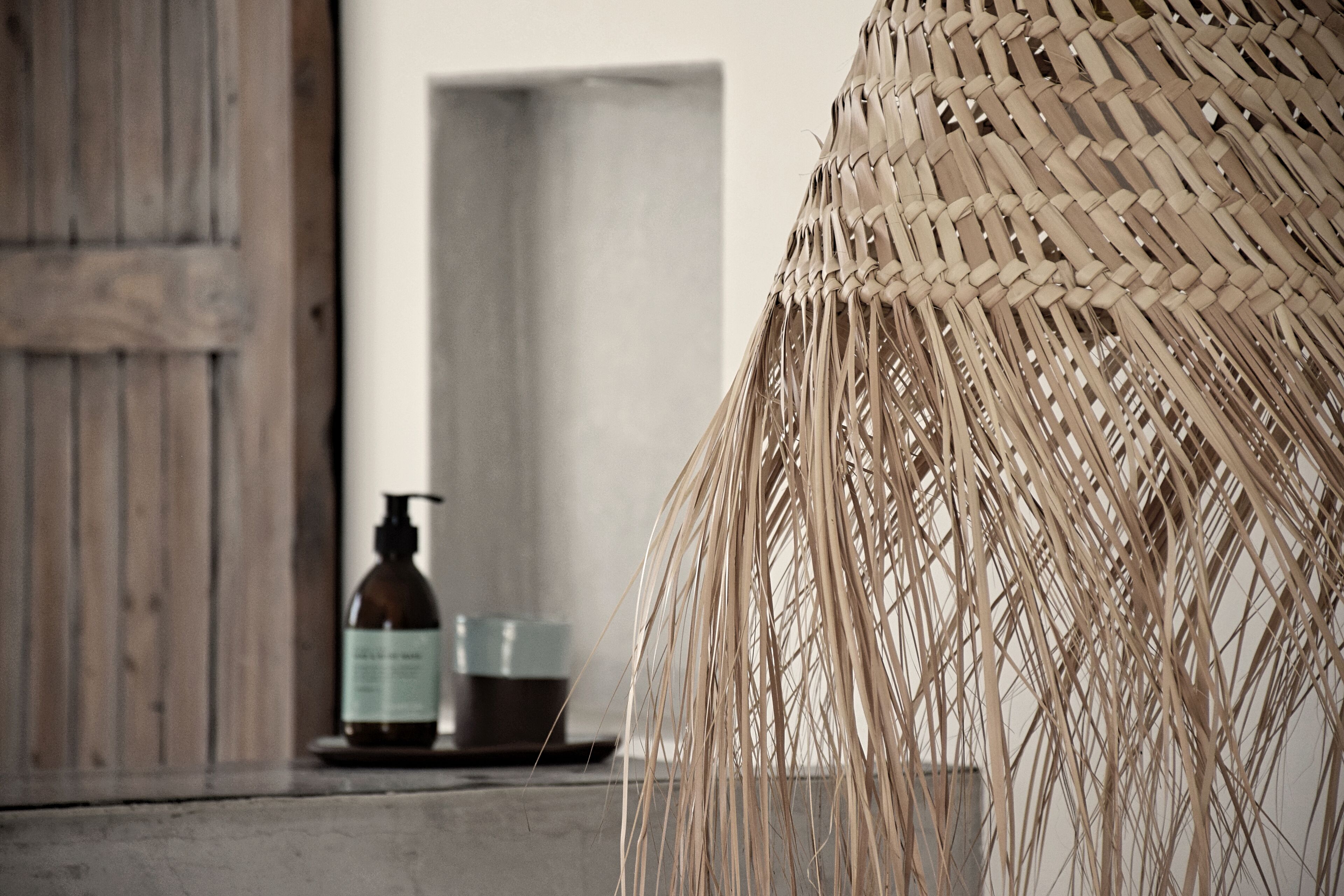 A room with a rustic wooden door, a woven basket, and a bottle of liquid soap on a table.
