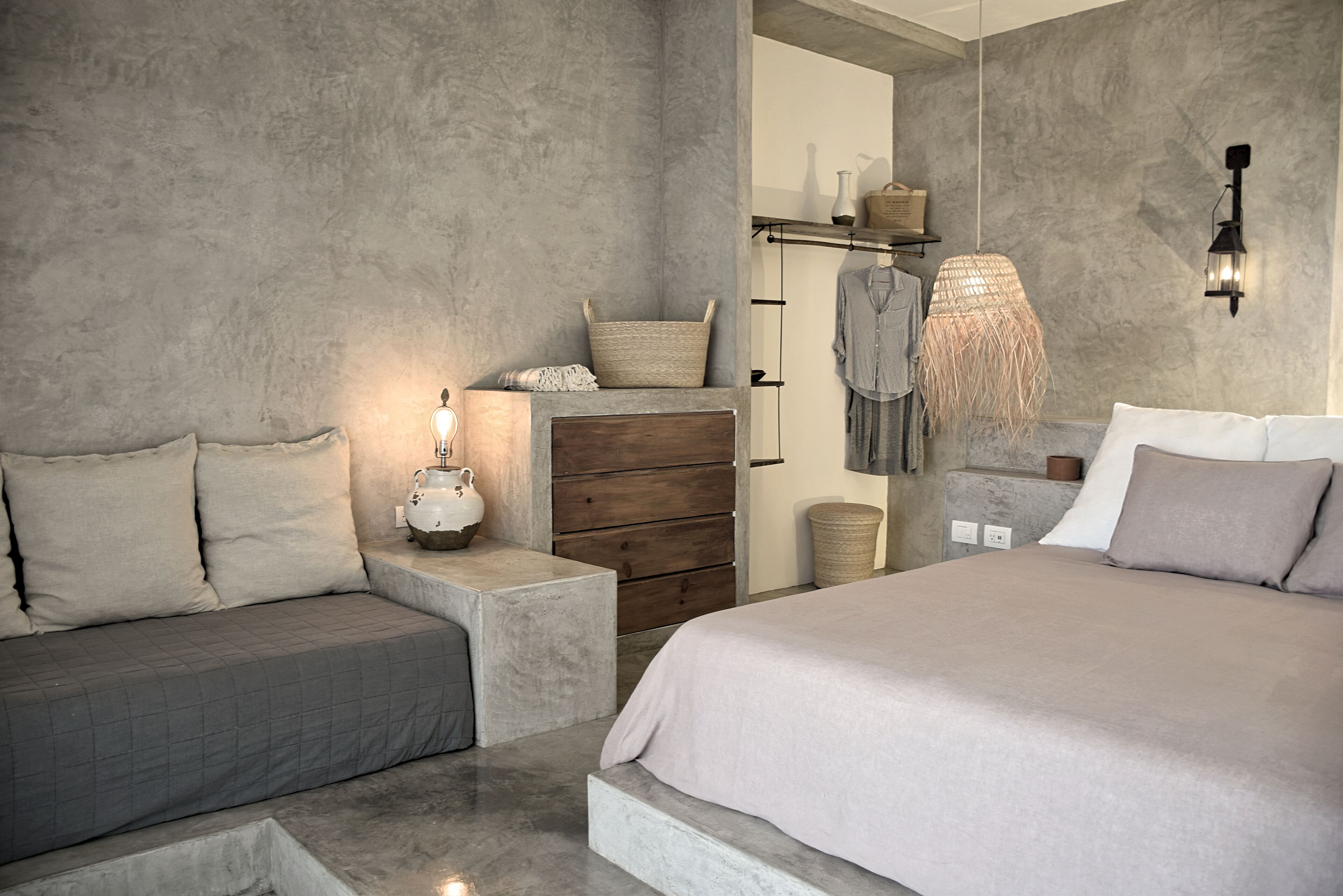 Quarto moderno com cama grande, sofá, cômoda e luminária suspensa.