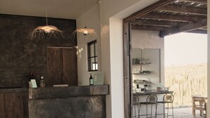 A modern kitchen with a dark countertop, two pendant lights, and a view of the desert through an open door. - Desierto Azul (Todos Santos)
