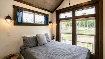A bedroom with a large bed, two windows, a nightstand, and a lamp.