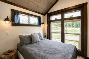 Un dormitorio con una cama grande, dos ventanas, una mesita de noche y una lámpara.
