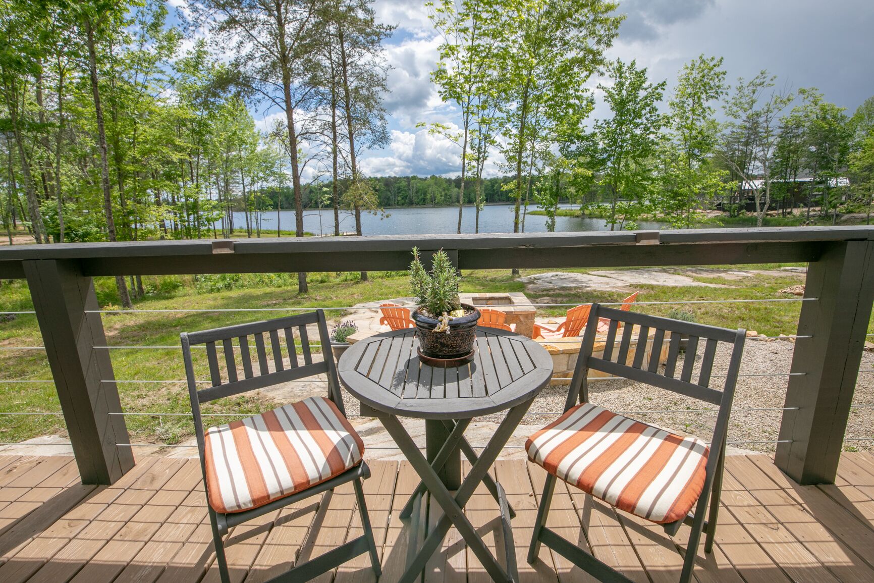 A wooden deck with two chairs and a table, overlooking a lake and surrounded by trees.