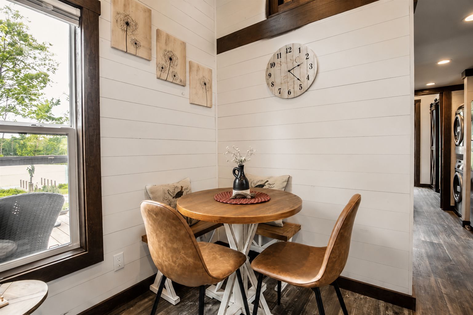 A dining area with a round table, four chairs, a clock, and artwork on the wall.