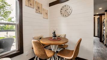 A dining area with a round table, four chairs, a clock, and artwork on the wall.