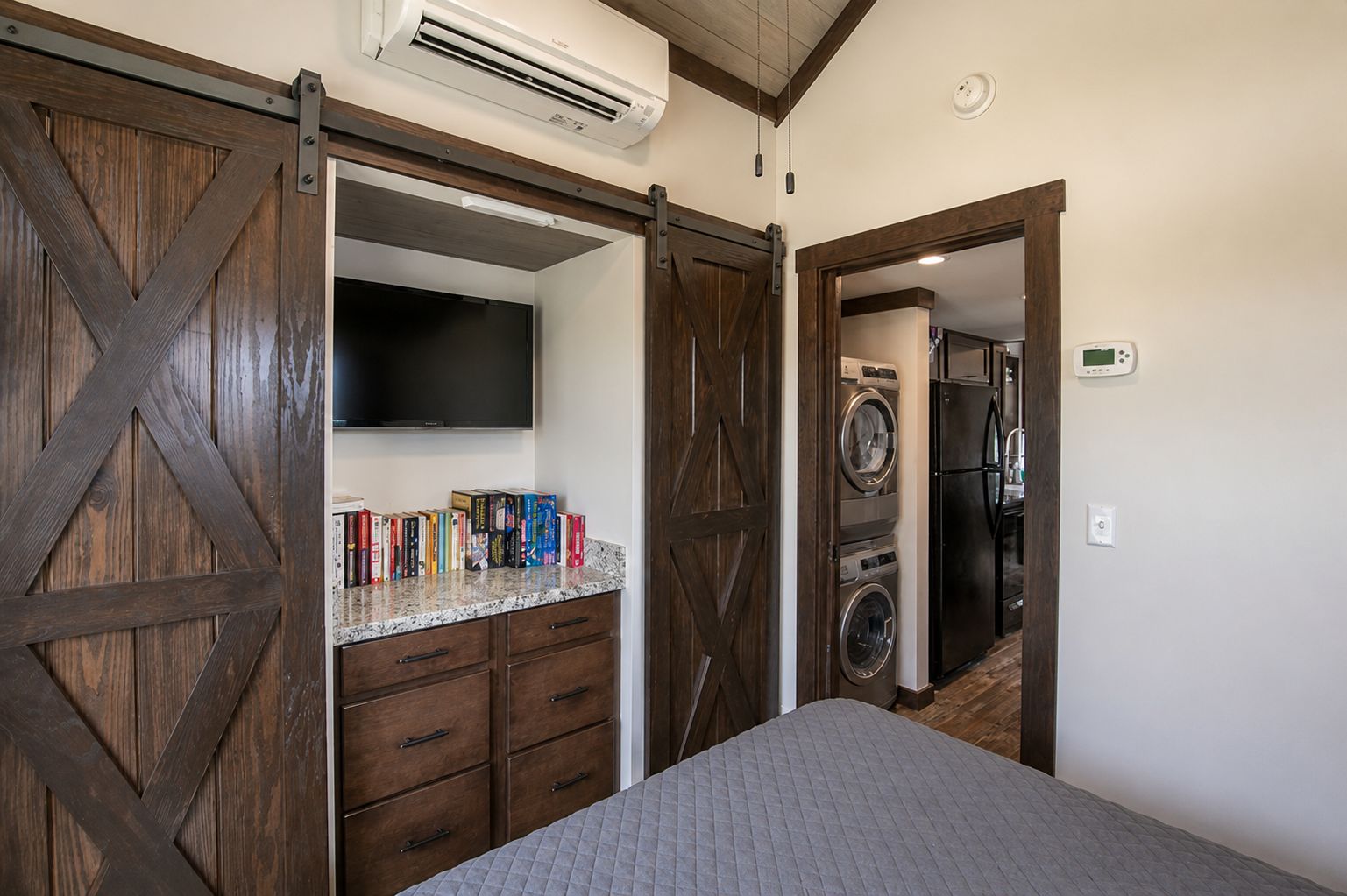 Une chambre à coucher comprenant un lit, un téléviseur, une bibliothèque et un espace buanderie avec des machines à laver.
