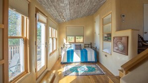A bedroom with a bed, a window, a wooden ceiling, and a staircase.