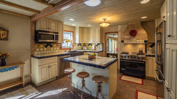 A kitchen with a central island, bar stools, a stove, and a microwave.