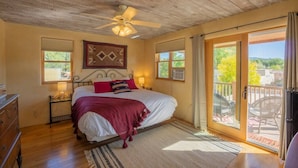 A bedroom with a bed, a ceiling fan, a window, a door leading to a balcony, and a dresser.