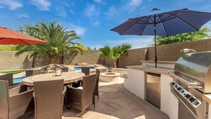 Un patio al aire libre con una mesa redonda, sillas de mimbre, una parrilla y una piscina.