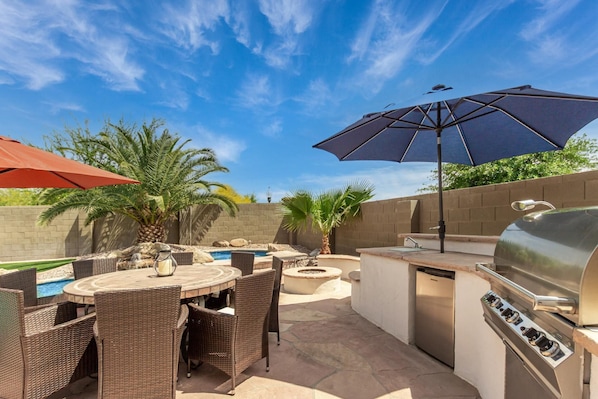 Une terrasse extérieure avec une table ronde, des chaises en osier, un barbecue et une piscine.
