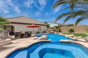 Un jardin avec une piscine, du mobilier de jardin et un espace barbecue.