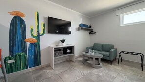 Una sala moderna con televisor de pantalla plana, un cuadro de cactus, un sofá, una mesita y una ventana.