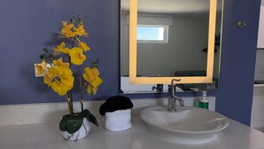 Un baño con un lavamanos blanco, un espejo y un florero con flores amarillas.