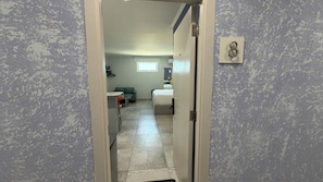 Un couloir menant à une chambre à coucher qui contient un lit, une chaise et une table.