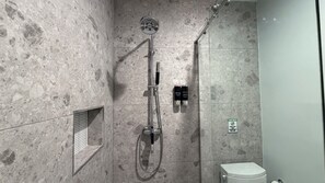 Moderni kylpyhuone, jossa on suihku, wc ja seinään upotettu hylly.