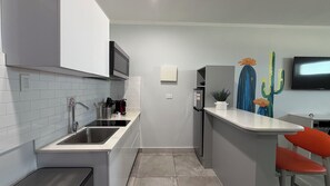 Eine kompakte Küche mit integriertem Mikrowellenherd, einer Edelstahl-Spüle und einem kleinen Kühlschrank.