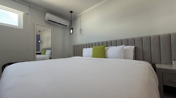 Hotellihuone, jossa on suuri sänky, yöpöytä, peili, ilmastointilaite ja ikkuna.