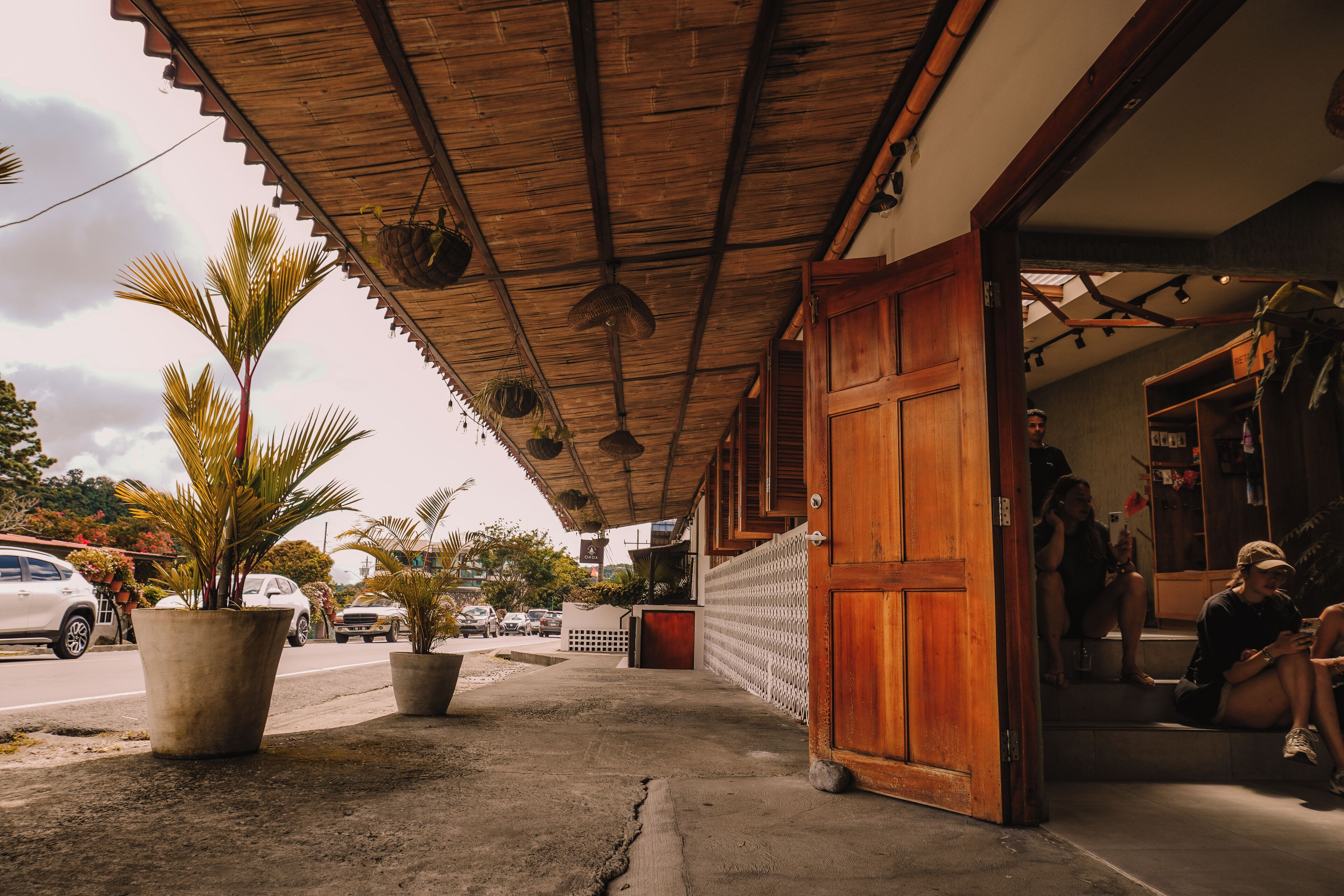 A building with a wooden door and a covered walkway. There are potted plants on the walkway.