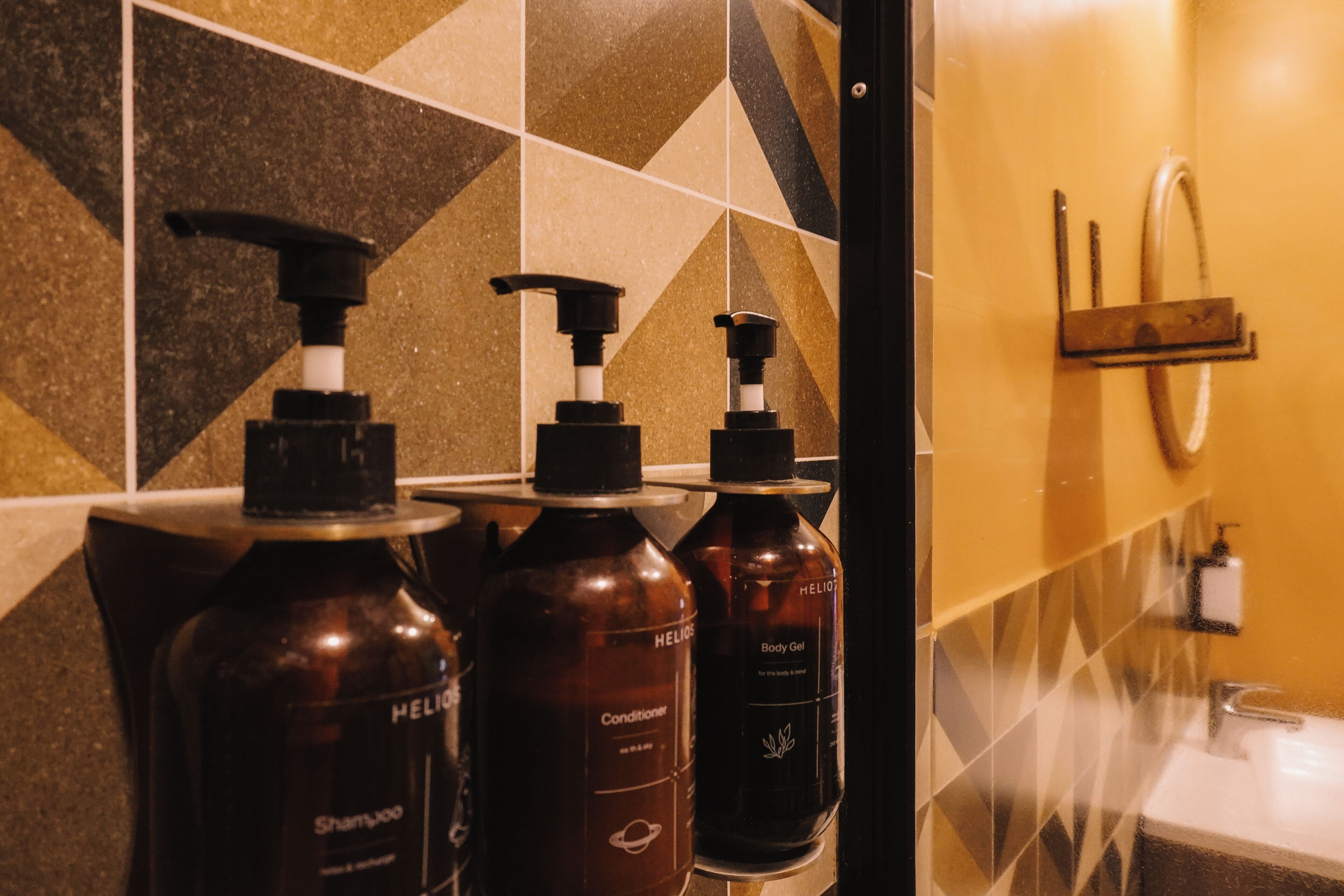 A bathroom with a tiled wall, a sink, and three bottles of shampoo and conditioner.