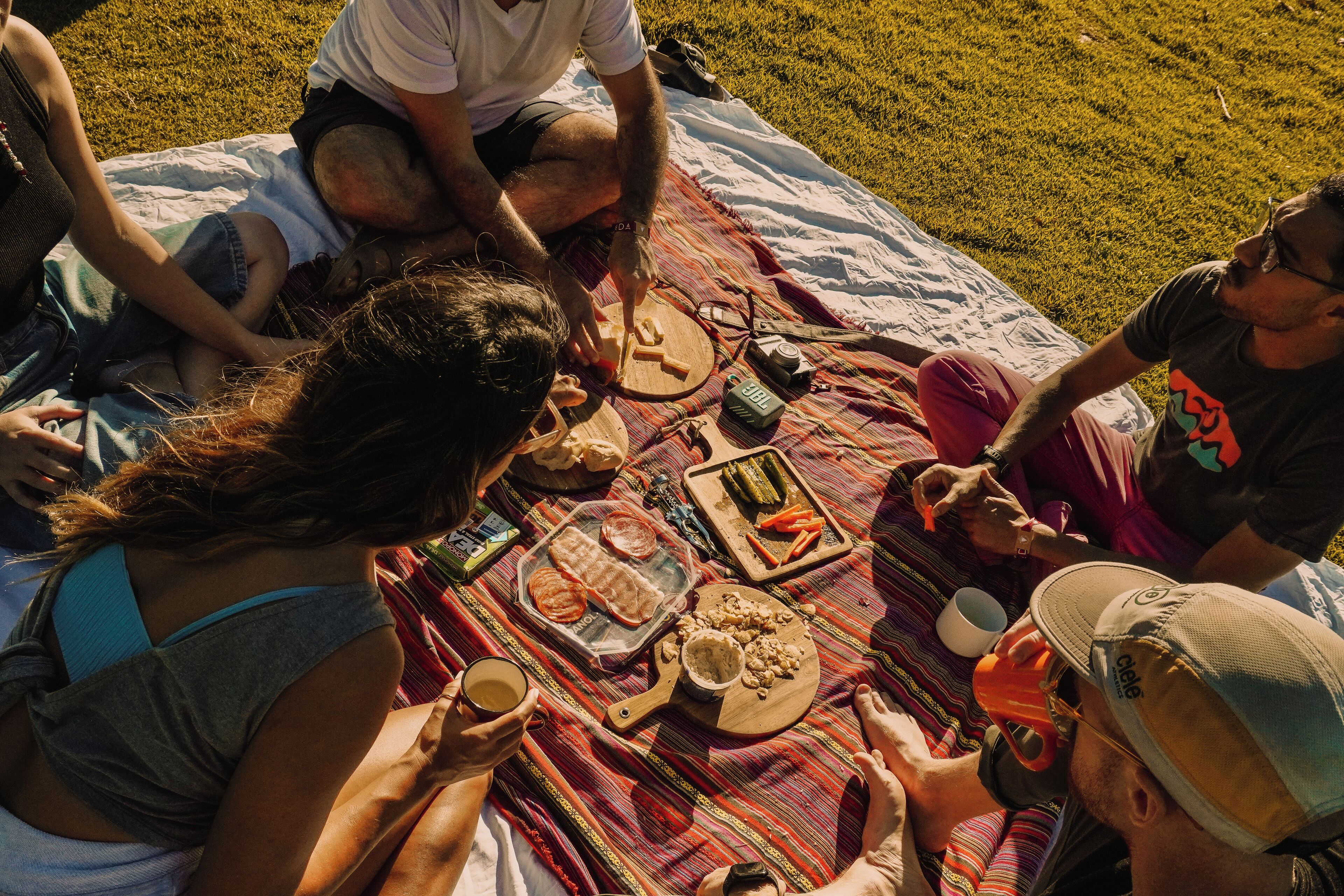 Un grupo de personas sentadas sobre una manta al aire libre, con comida y bebidas.