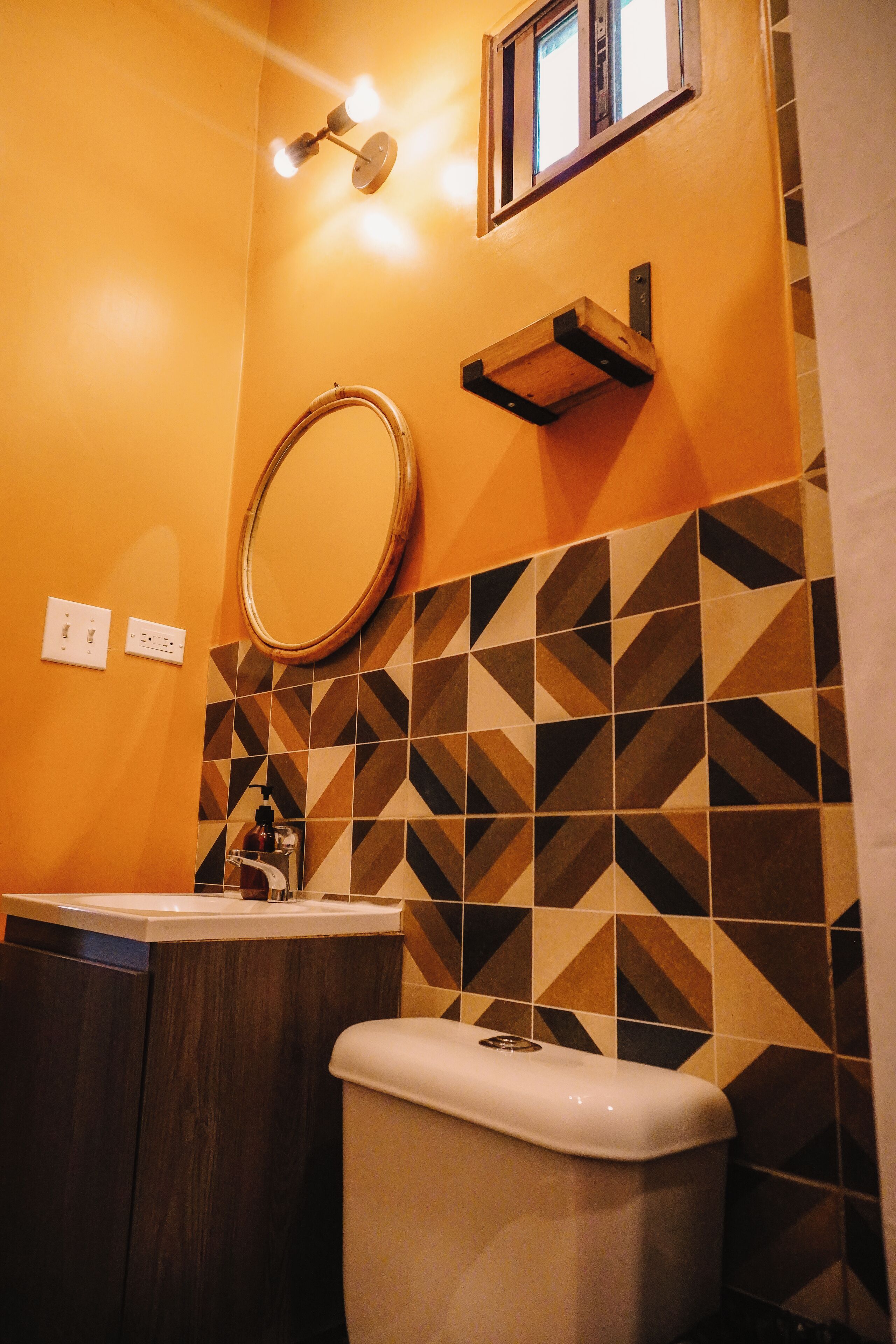 Une salle de bain équipée de toilettes, d’un lavabo, d’un miroir et de carreaux aux motifs géométriques.