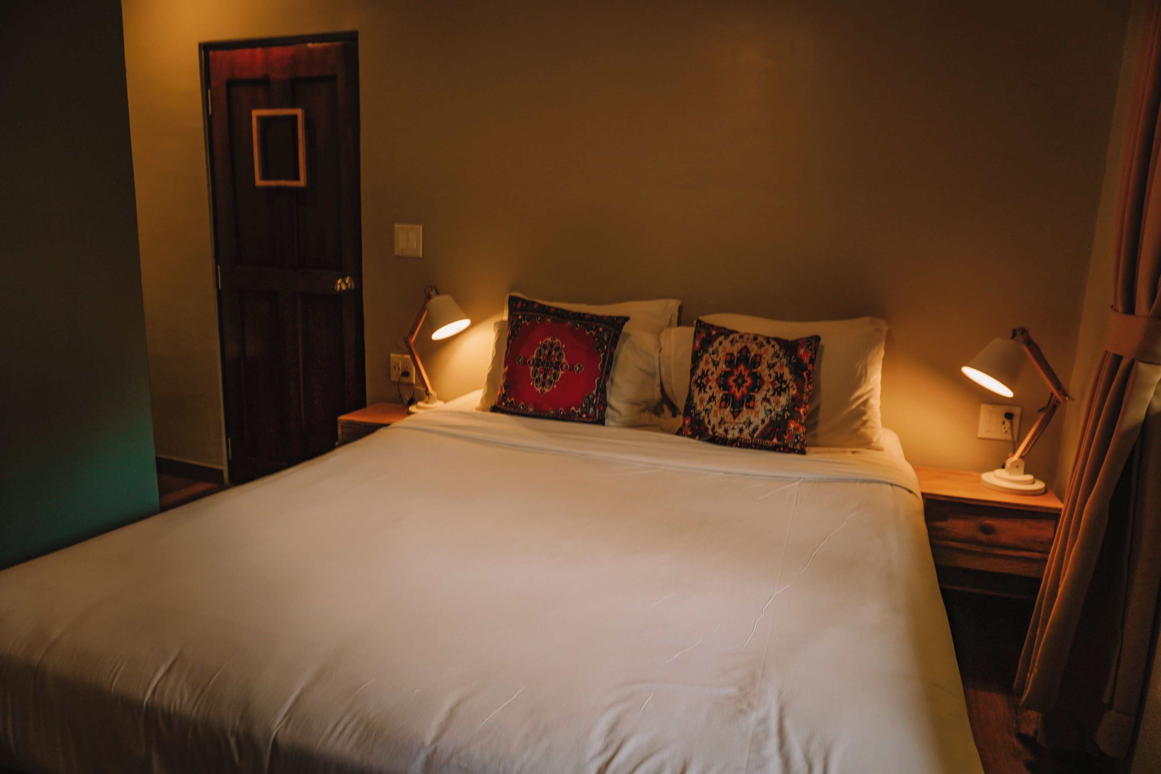 A neatly made bed with white linens and decorative pillows, two bedside lamps, and a wooden door.